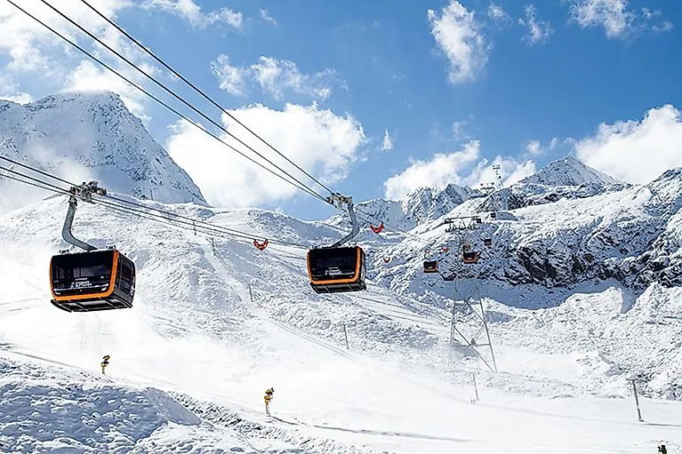 Die moderne 3S-Eisgratbahn fährt durch die verschneite Berglandschaft des Stubaier Gletschers unter blauem Himmel.