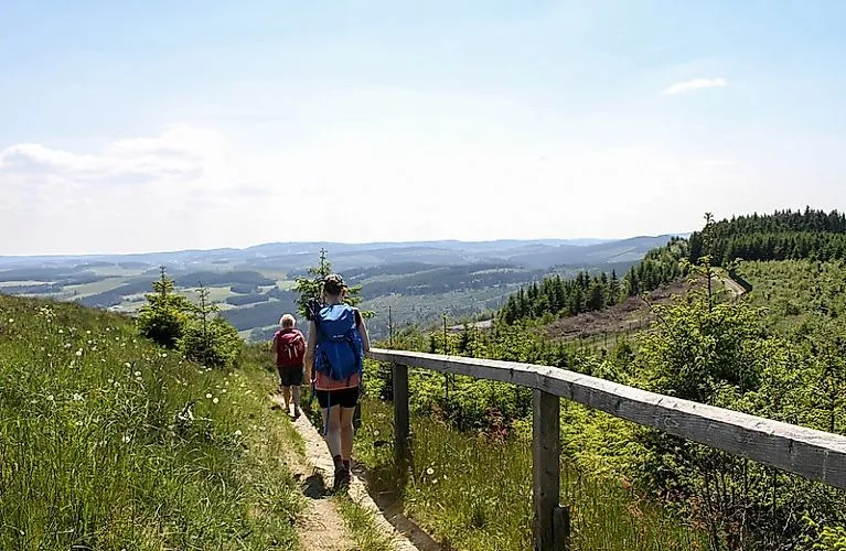 Zwei Wanderer auf einem Pfad bei Winterberg im Sauerland mit weitem Blick über grüne Hügel und Wälder an einem Sommertag