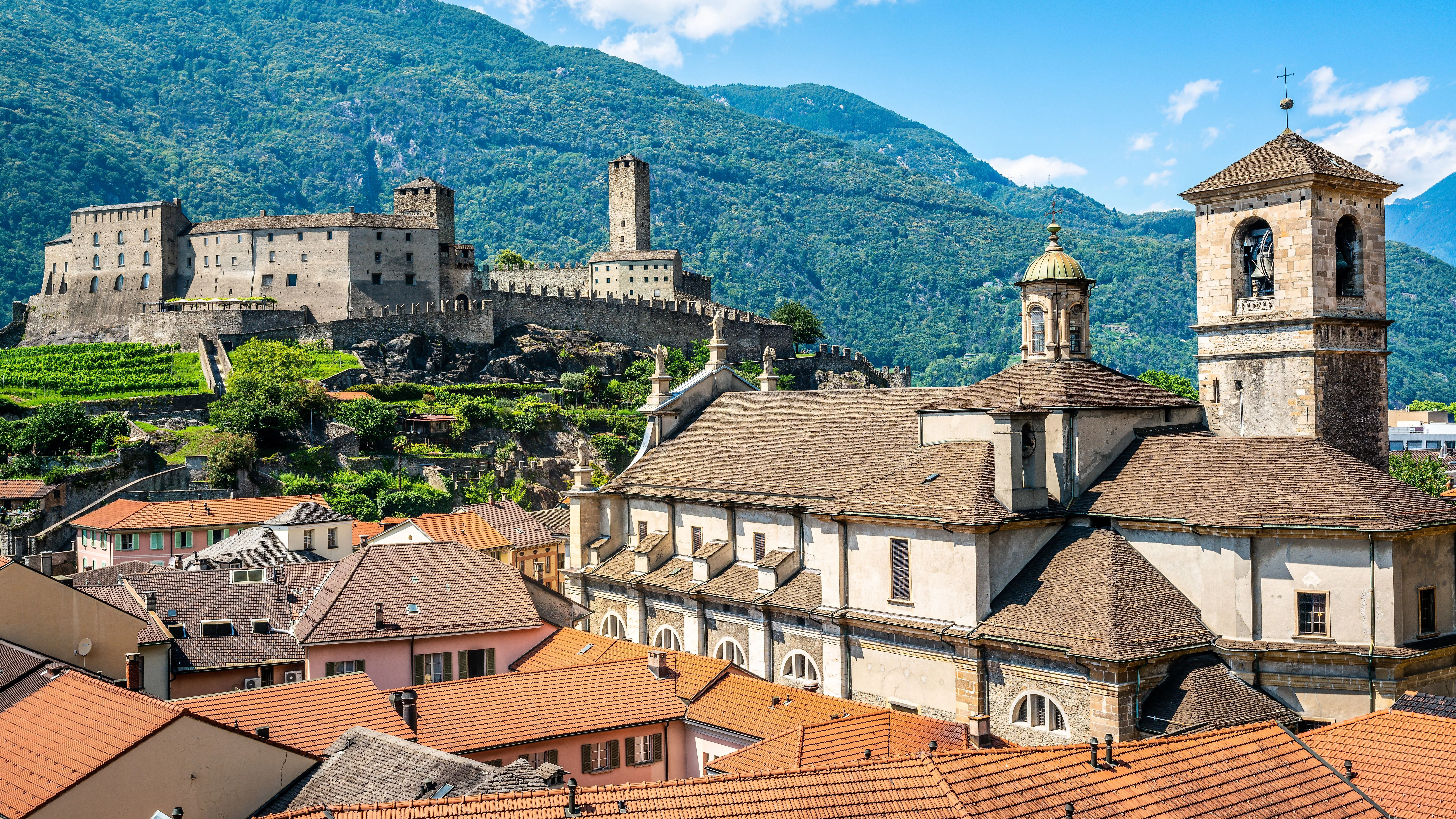 Lo storico Castelgrande a Bellinzona, in Svizzera, sullo sfondo di montagne verdi e tetti rossi.