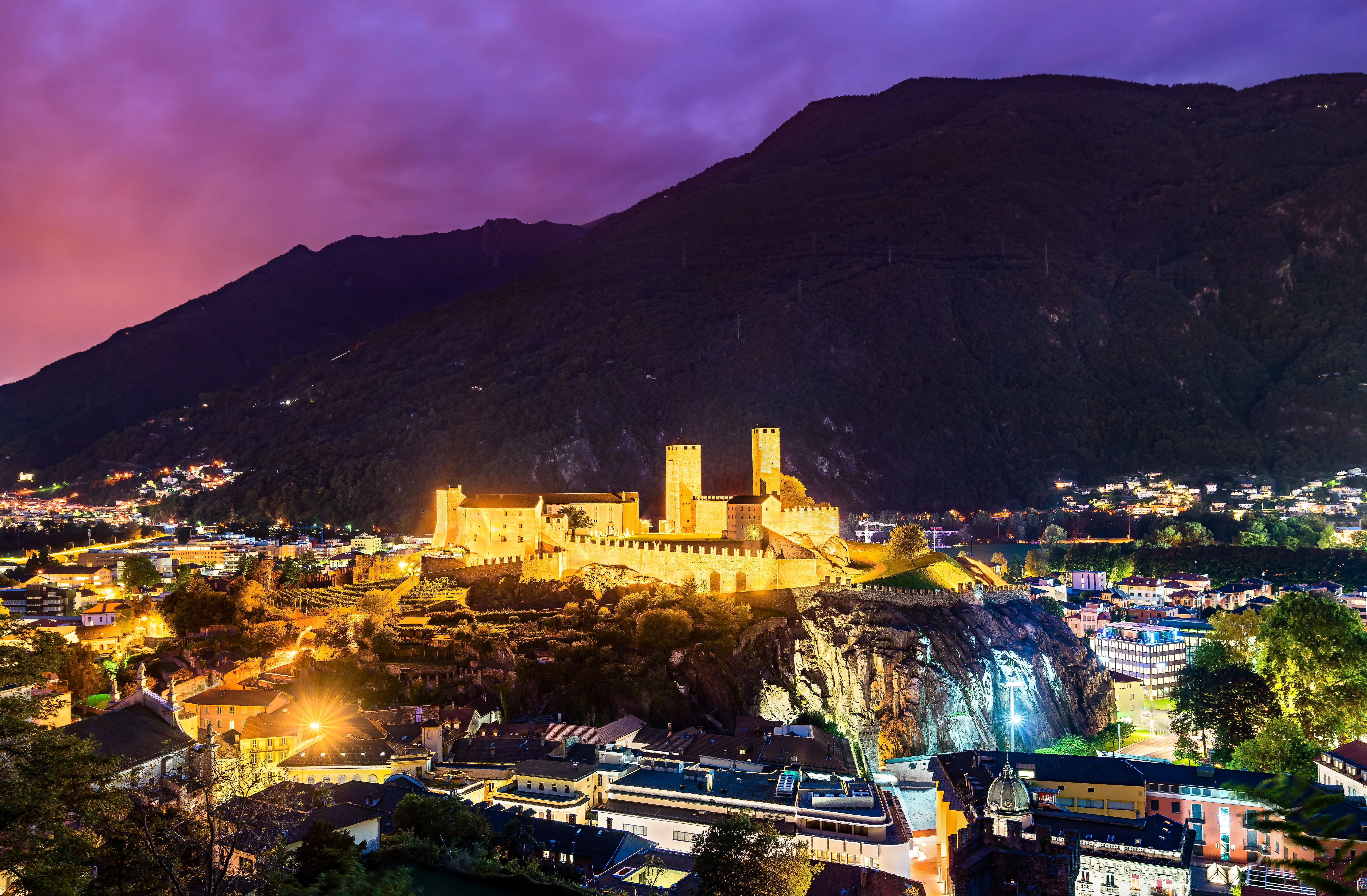 Castelgrande a Bellinzona di notte, illuminato a festa davanti alle scure pendici delle montagne e al cielo serale