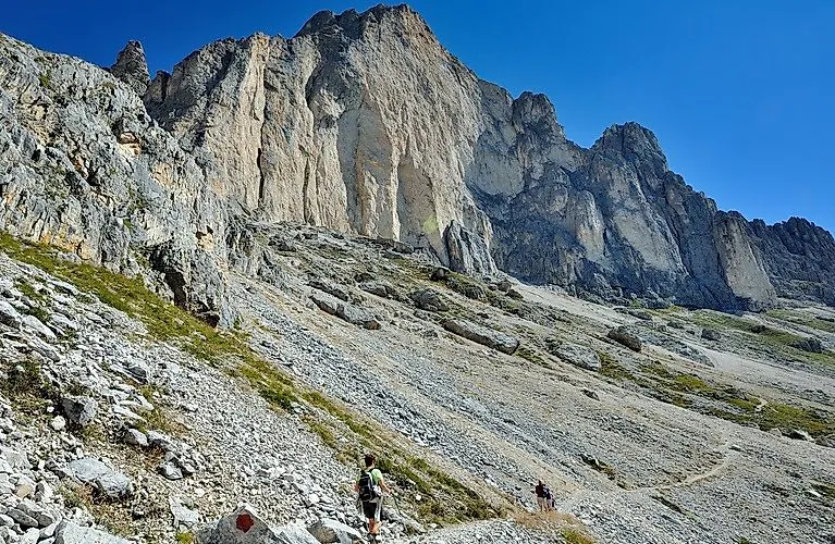 Wanderer unterhalb imposanter Felswände in Carezza in den Dolomiten bei strahlendem Sommerwetter