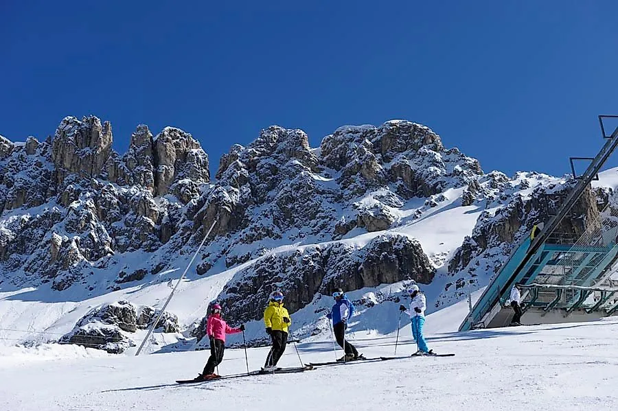 Skigruppe auf sonniger Piste im Skigebiet Carezza vor beeindruckender Felskulisse