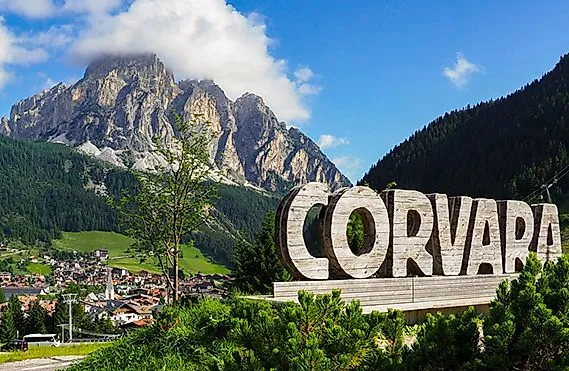 Aussicht auf das Dorf Corvara im Sommer, umgeben von grünen Wiesen und den beeindruckenden Gipfeln der Dolomiten.
