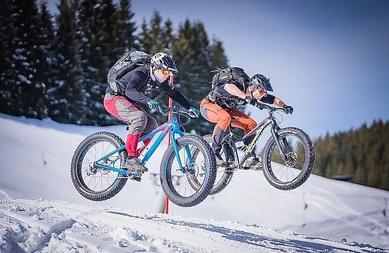 Zwei Biker springen mit Fatbikes im Schnee auf der Postalm
