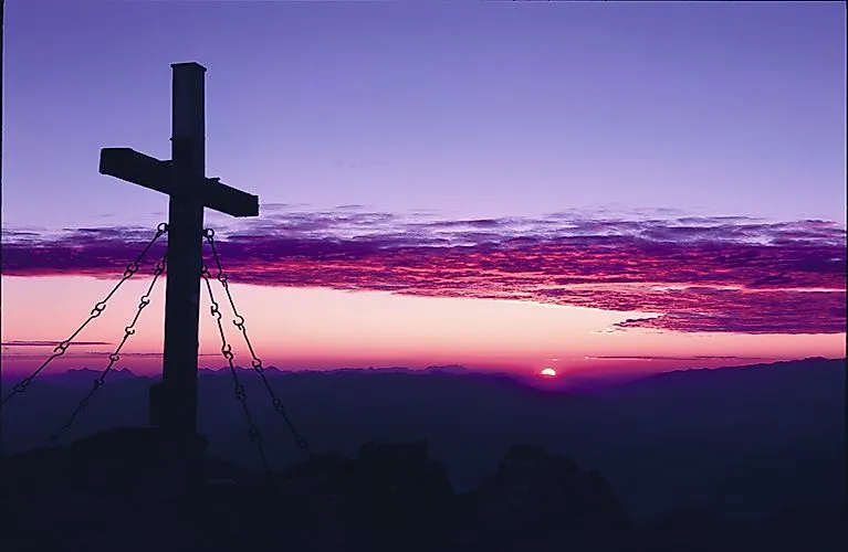 Gipfelkreuz bei Sonnenaufgang in den Tiroler Alpen mit spektakulärem Farbenspiel am Himmel