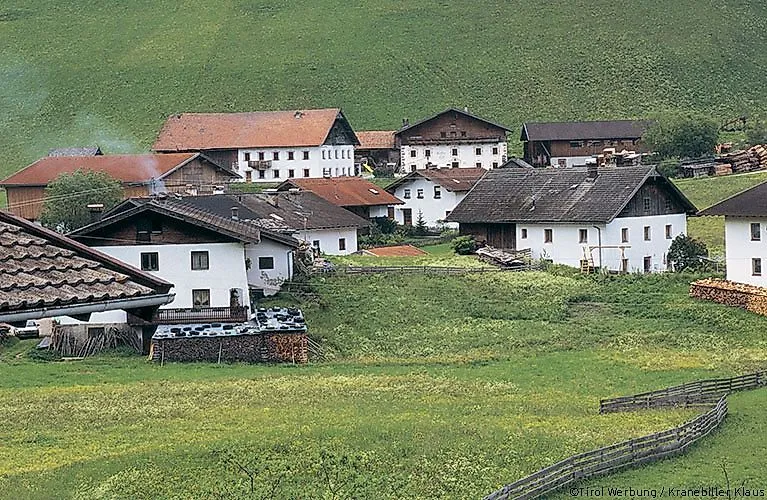 Tradizionale villaggio tirolese con casali storici a Obernberg am Brenner, circondato da prati verdi ai piedi di una collina.