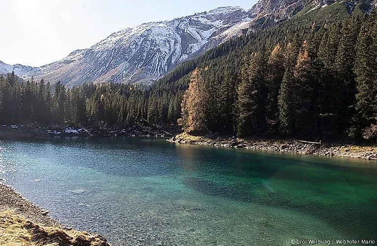 Il lago di Obernberg con acque blu turchese, circondato da fitte foreste e montagne innevate nella valle Wipptal.