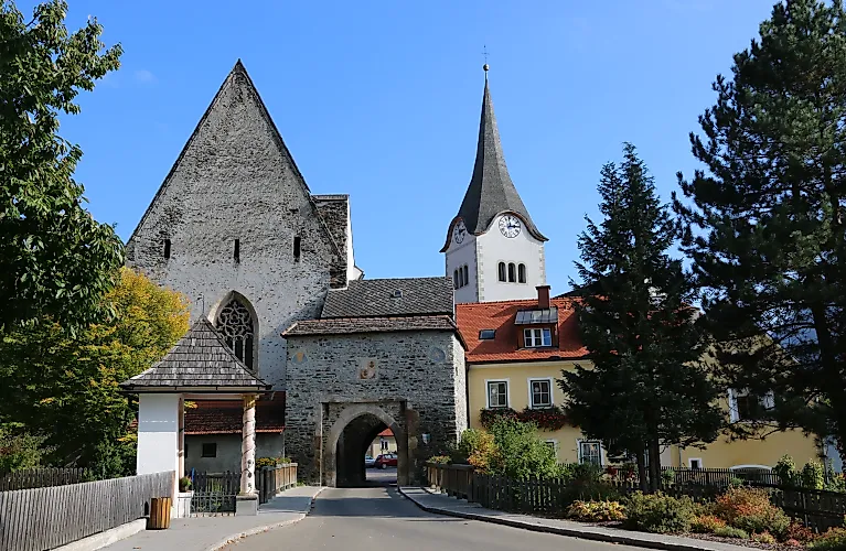 Mittelalterliches Hintereggertor mit Kirche und bunten Häusern in Oberwölz an einem sonnigen Sommertag.