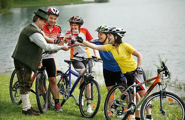 Gruppe von Radfahrern stößt mit einem Steirer auf einer Radtour bei einem See in Bad Radkersburg an.