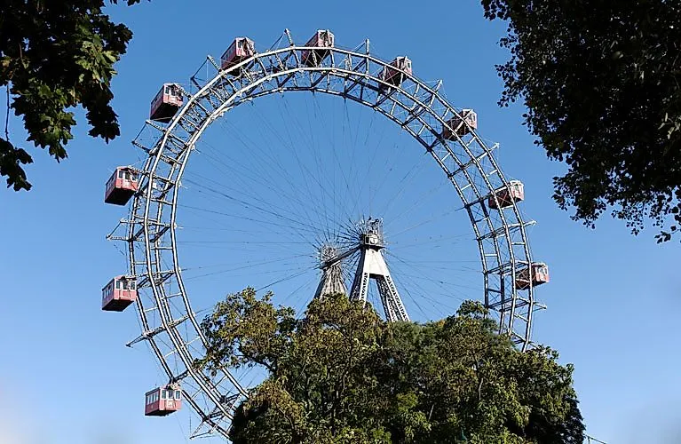 La ruota panoramica di Vienna al Prater, sotto un cielo azzurro e circondata da alberi: il simbolo della città e l'attrazione preferita.