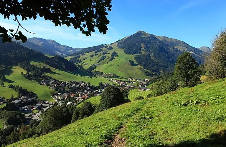 Sommerpanorama von Saalbach mit Blick auf den Zwölferkogel und grüne Almwiesen unter blauem Himmel.