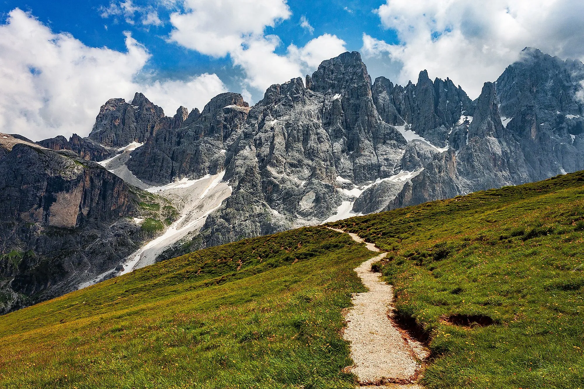 Wanderweg auf einer grünen Alm vor der beeindruckenden Felskulisse von San Martino di Castrozza in den Dolomiten.