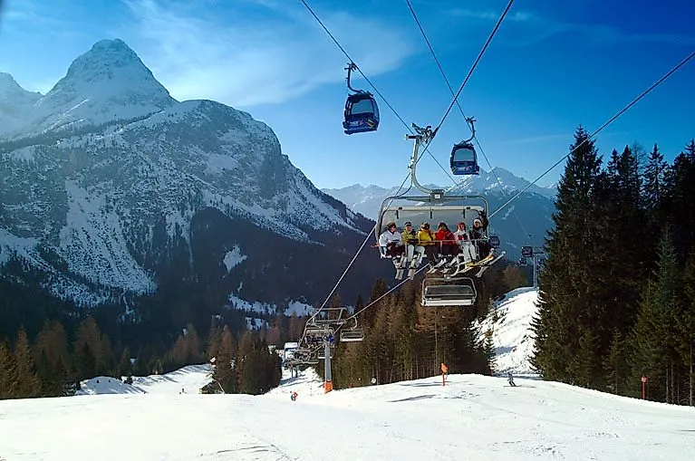 Menschen auf einem Sessellift beim Skifahren in Ehrwald mit Blick auf die verschneite Zugspitze und umliegende Bergwelt.