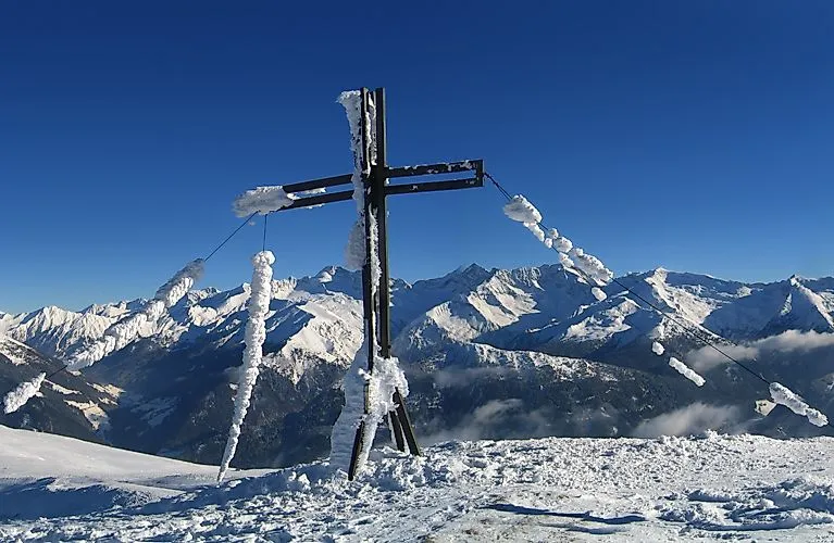 Verschneites Gipfelkreuz mit imposanter Aussicht auf die Tiroler Alpen bei klarem Winterwetter in Steinach.
