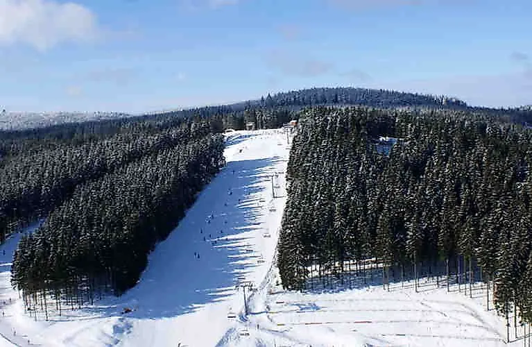 Breite Skipiste im verschneiten Skigebiet Winterberg umgeben von dichten Wäldern bei sonnigem Winterwetter