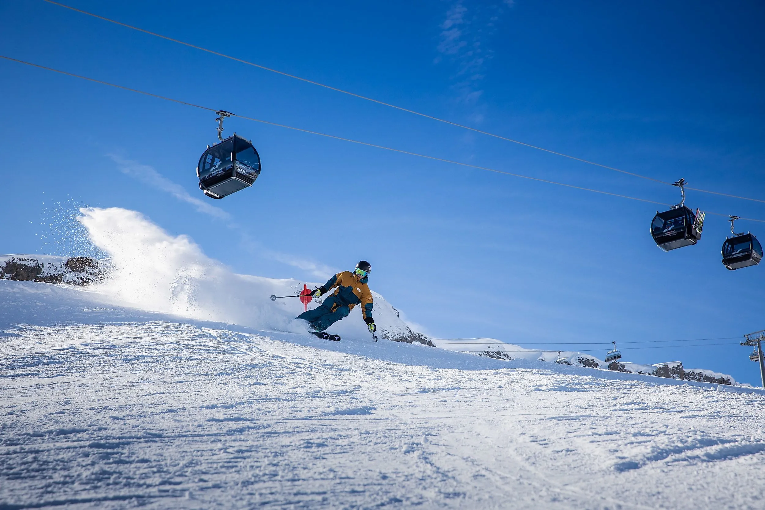 Skifahrer bei Abfahrt im Skigebiet Ifen im Kleinwalsertal unter moderner Gondelbahn