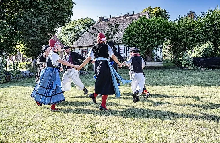 Menschen in traditionellen Trachten tanzen vor einem reetgedeckten Haus in Mönchgut auf Rügen.