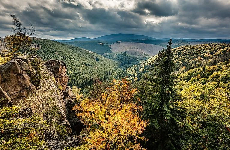 Blick über herbstlich gefärbte Wälder und Felsen im Harzgebirge unter dramatischem Himmel.