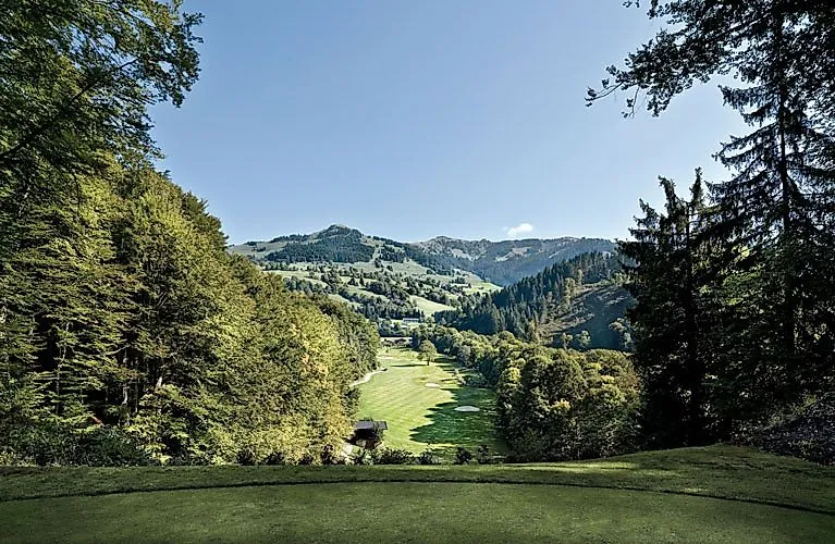 Blick auf ein gepflegtes Tal mit einem Golfplatz, eingerahmt von dichten grünen Wäldern und sanften Hügeln in der Umgebung von Kitzbühel.