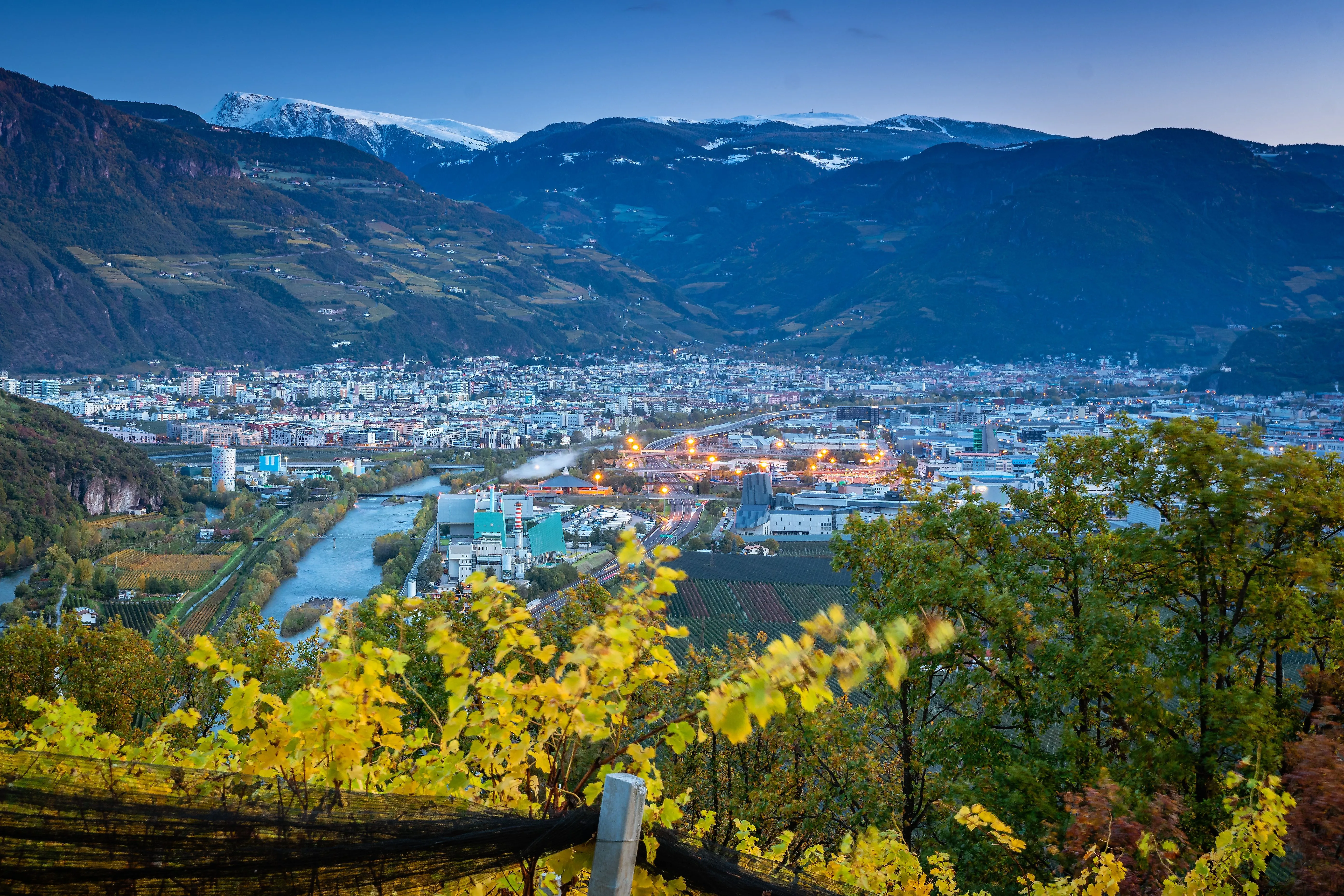 Blick auf Bozen in Südtirol mit Etsch, Weinbergen und Bergpanorama in der Abenddämmerung