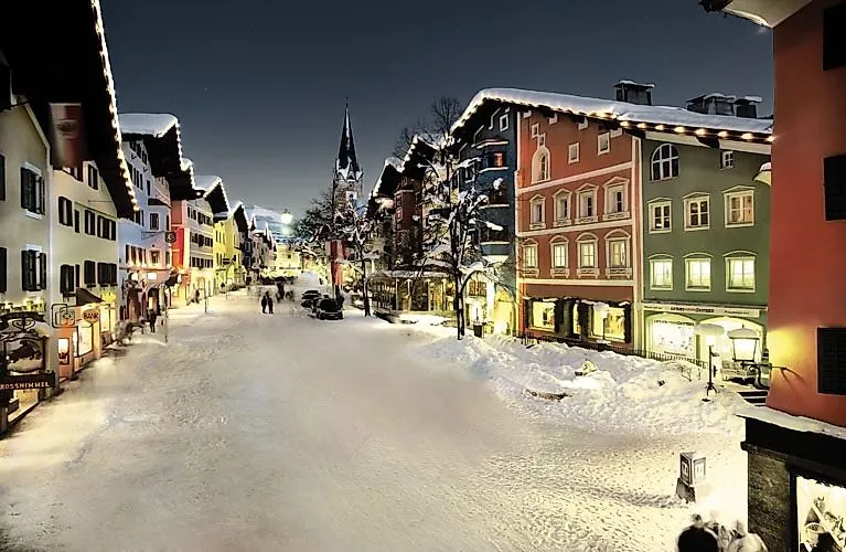 Abendliche Winterstimmung in der historischen Altstadt von Kitzbühel mit beleuchteten Häuserfassaden, verschneiten Straßen und Menschen beim winterlichen Stadtbummel.