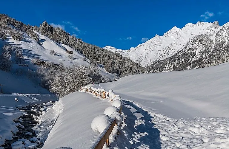 Tief verschneiter Winterweg in Gossensass mit Blick auf die schneebedeckten Alpen.