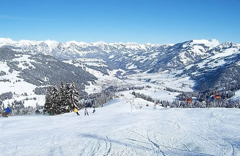 Wintersporters op een brede skipiste in Zweisimmen met besneeuwde bergtoppen op de achtergrond.