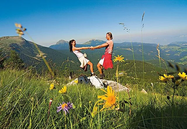 Paar genießt Wanderpause auf Almwiese mit Bergblick in Obereggen, Südtirol