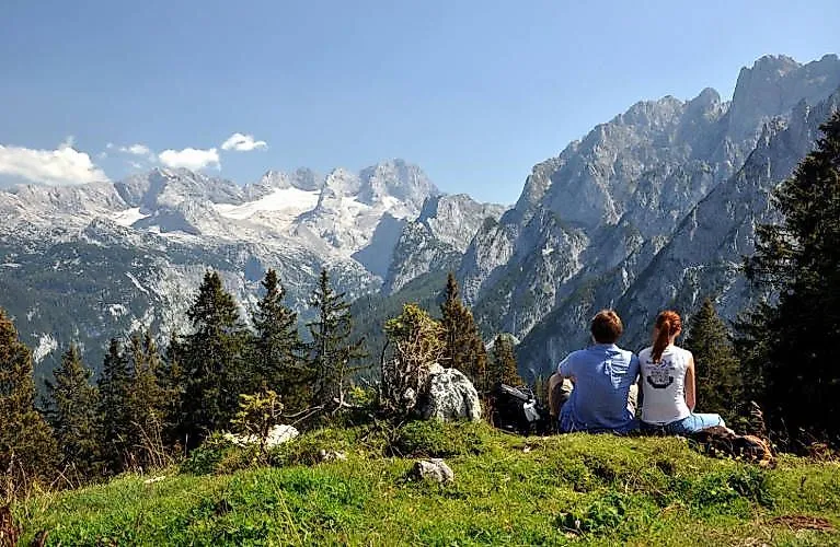 Two hikers enjoy the view of the imposing mountains of the Dachstein massif near Gosau on a sunny summer's day.