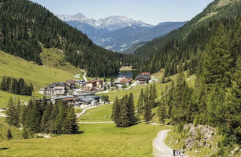 Panorámica estival del Zauchensee con pueblo de montaña, verdes prados alpinos y rutas de senderismo