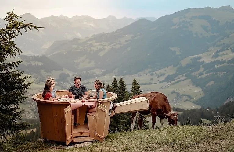 Een groep fijnproevers geniet buiten van een fondue met een panoramisch uitzicht op de groene hellingen van de Rinderberg in Zweisimmen.