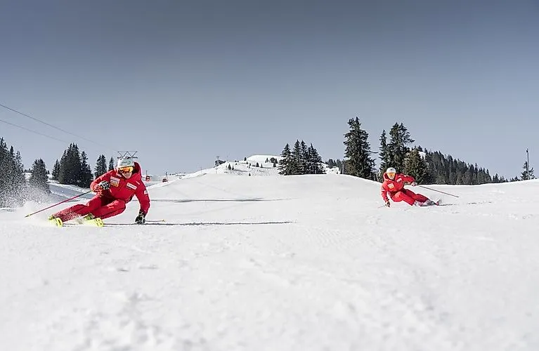 Twee skileraren in rode pakken tijdens een snelle afdaling op een perfect geprepareerde piste in Zweisimmen.